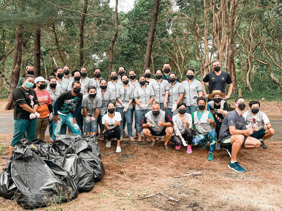 Group of associates posing together with black trash bags in a wooded area have a clean-up event.